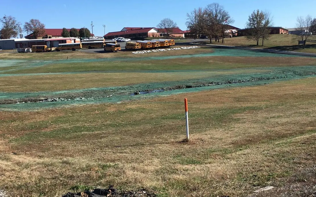 A large school field at South Side High School freshly hydroseeded, the new green slurry visible over the graded soil